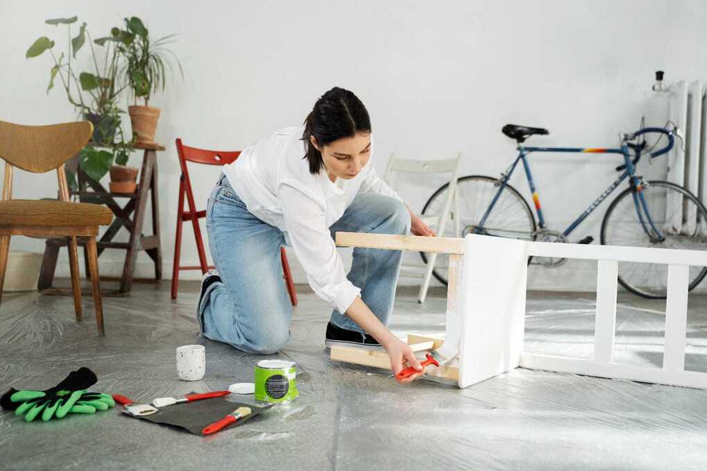 Une femme peint un meuble en bois blanc dans un espace intérieur, illustrant les "Tendances de rénovation durable 2025